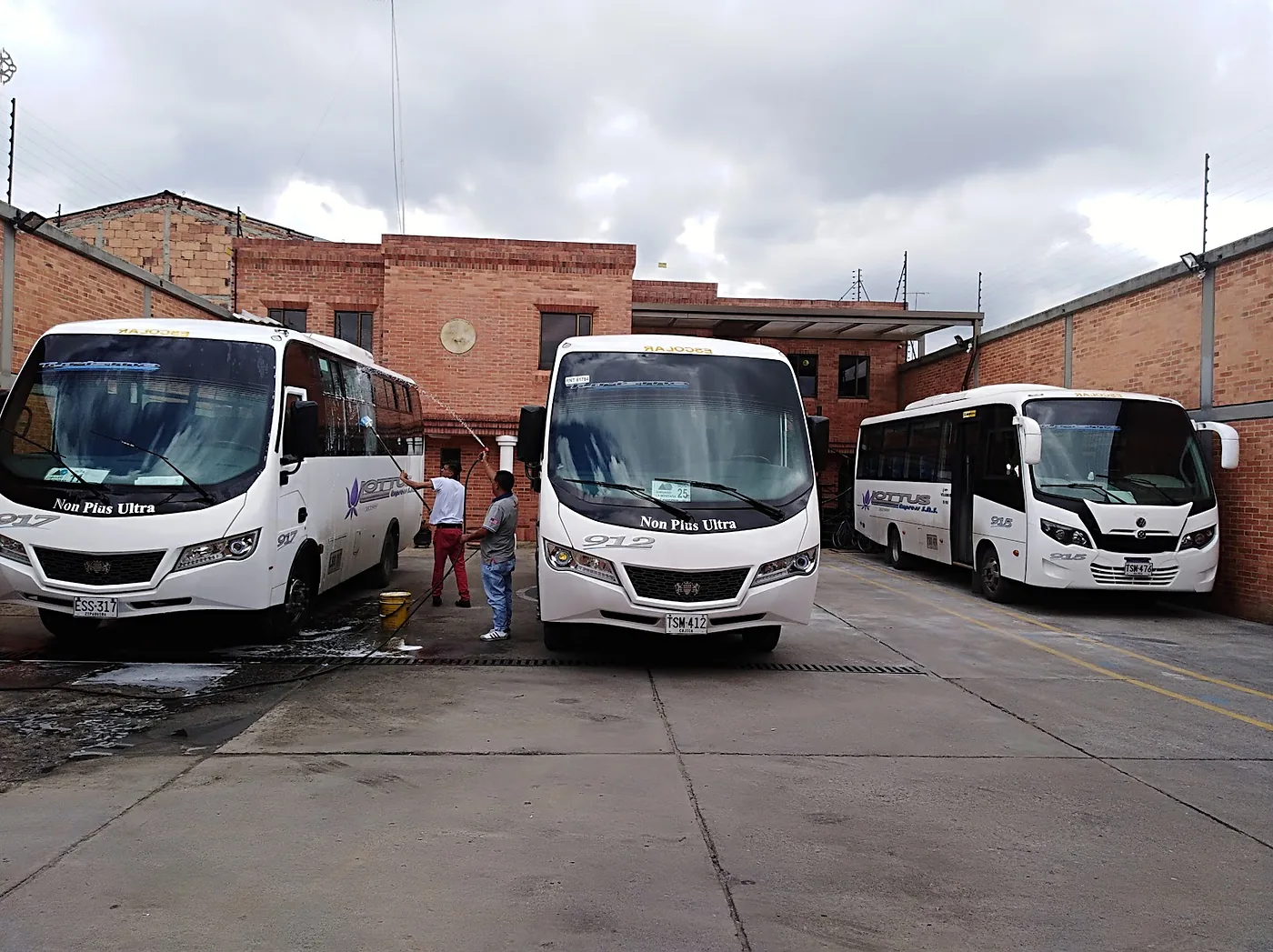 Dos operarios de Lottus Express lavan con manguera tres microbuses marcados ESCOLAR, en el patio propio de la Calle 163